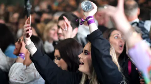 Getty Images A young female clubber points her phone towards the stage, surrounded by other clubbers