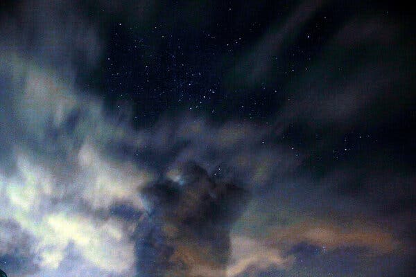 A meteor shower at night with a layer of clouds reflecting light below in a long exposure photograph.