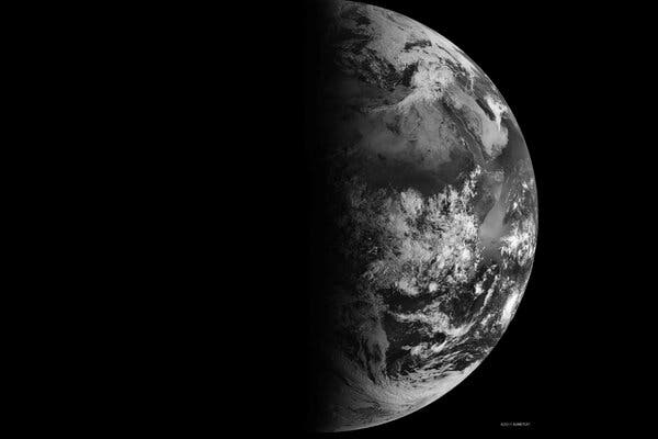 Half of Earth is visible in black and white on the right, with the rest of the planet in shadow.