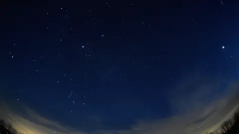 Getty Images A stunning wide-angle nighttime photograph of the evening sky, featuring four planets. 

Mars on the left, Jupiter in the middle, and Saturn and Venus on the right. Wispy clouds stretch across the lower part of the sky, with the silhouettes of trees and city lights glowing faintly. 