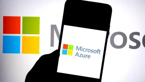 Getty Images A silhouetted hand holding a phone with the words "Microsoft Azure" on it. In the background is the red, green, blue and yellow Microsoft logo.